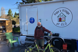 A person with a bicycle stands in front of a trailer housing Hope's Village of San Luis Obispo mobile showers