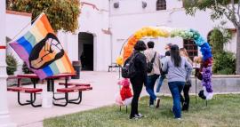 people walk under a rainbow balloon arch near an LGBTQ+ Pride flag