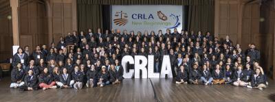 Staff of California Rural Legal Assistance lined up in front of a stage with large white letters CRLA and a white banner hanging in background