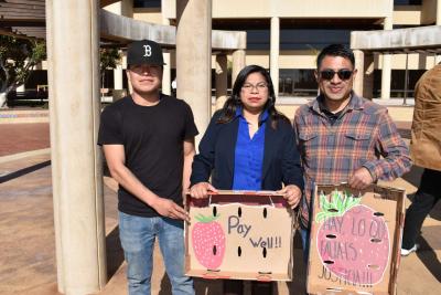 three people stand in front of concrete columns holding signs about fair wages