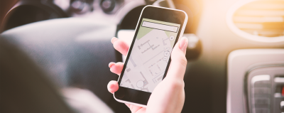A hand holding a phone with a map app on the screen.