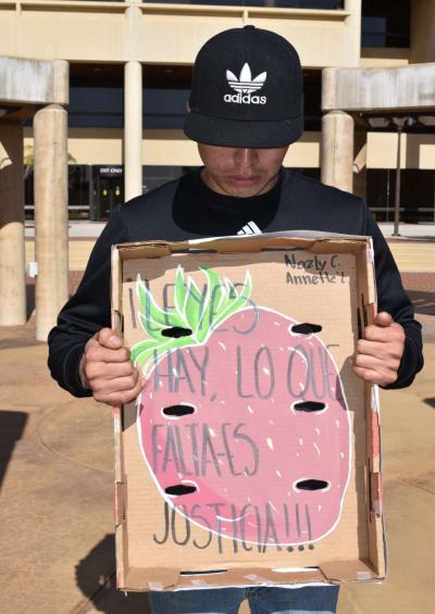a person looks down while holding a handpainted sign that reads "Leyes hay, lo que falta es justicia"