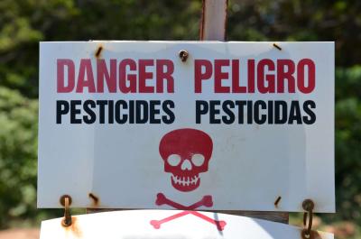 sign with skull and crossbones stating danger pesticides in English and Spanish