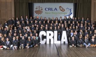 Staff of California Rural Legal Assistance lined up in front of a stage with large white letters CRLA and a white banner hanging in background