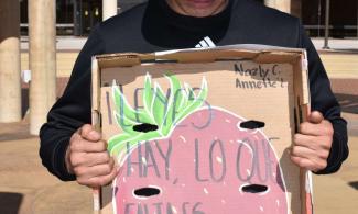 a person looks down while holding a handpainted sign that reads "Leyes hay, lo que falta es justicia"